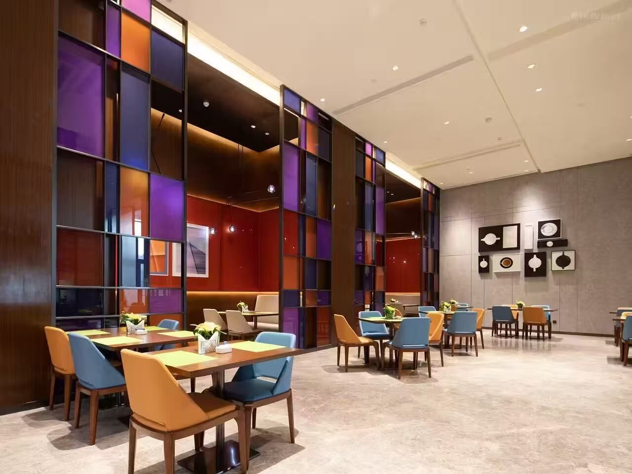 A modern dining area with tables and chairs, a wall with framed pictures, and a wooden partition with illuminated panels.