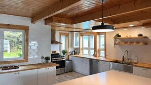 Een moderne keuken met witte kasten, een groot keukenblok, houten balken en een hangende lamp.