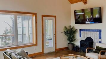 A spacious living room with a high ceiling, a large flat-screen TV mounted on the wall, a leather sofa, a wooden coffee table, and a potted plant.