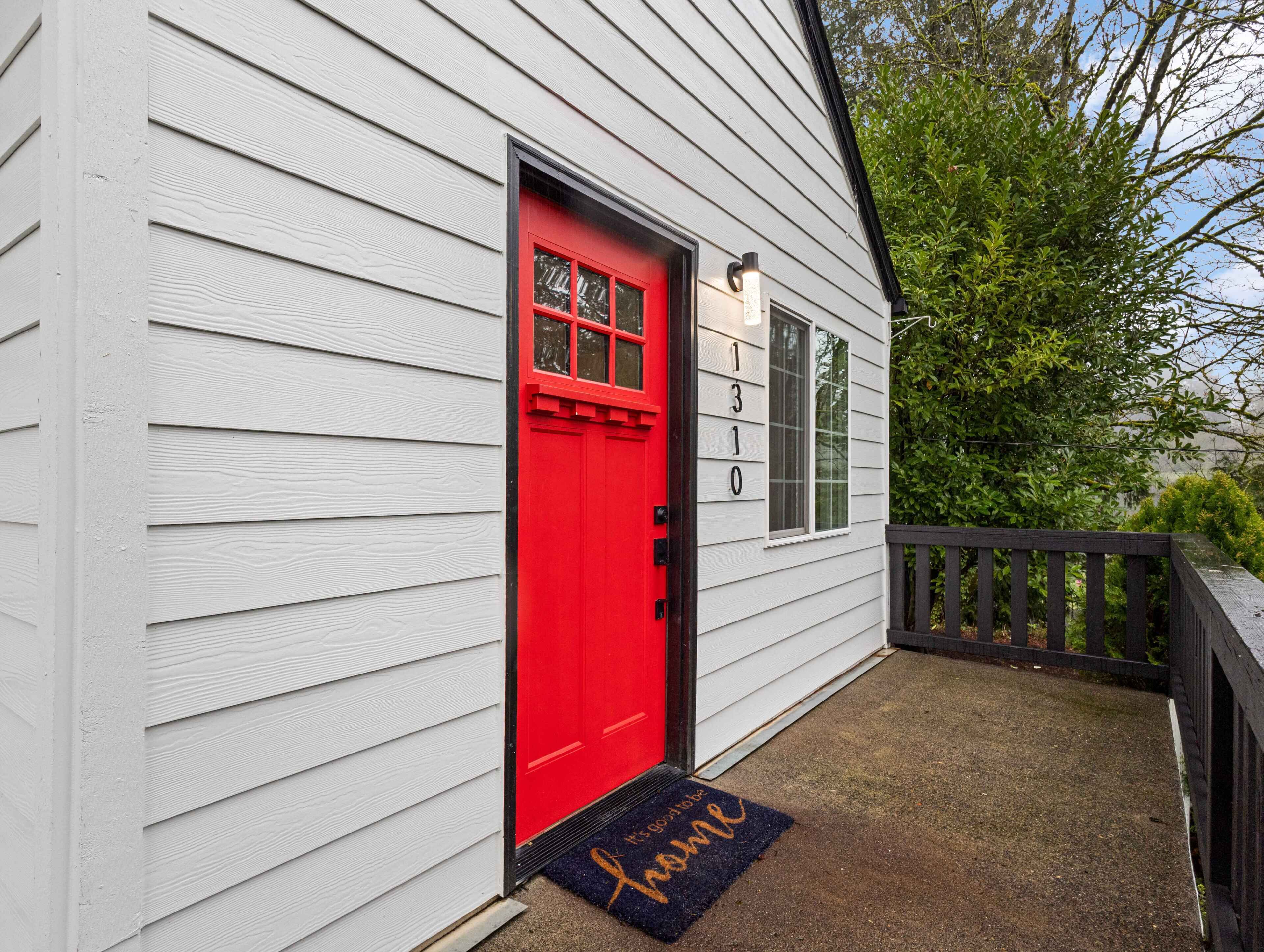 A white house with a red door, a black mailbox, and a doormat with 'Home' written on it.