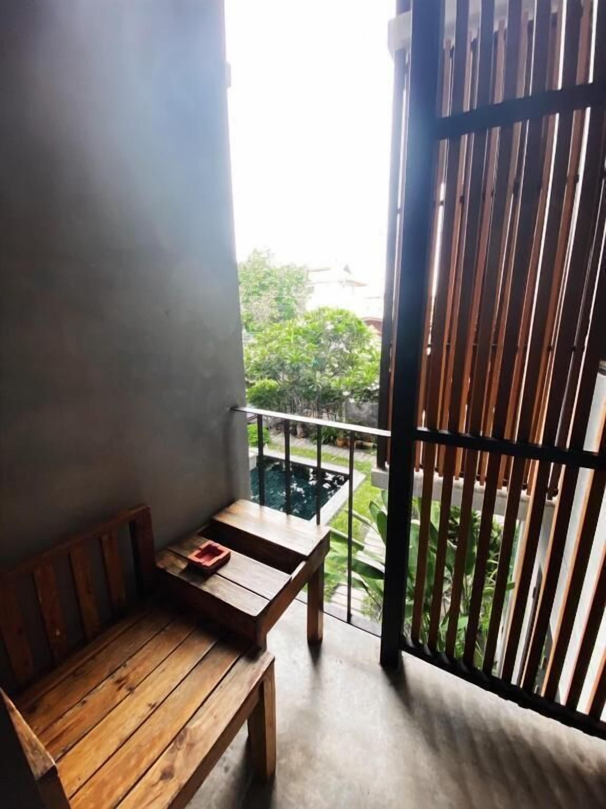 Een balkon met een houten bank en tafel, een metalen hekwerk en uitzicht op groen.