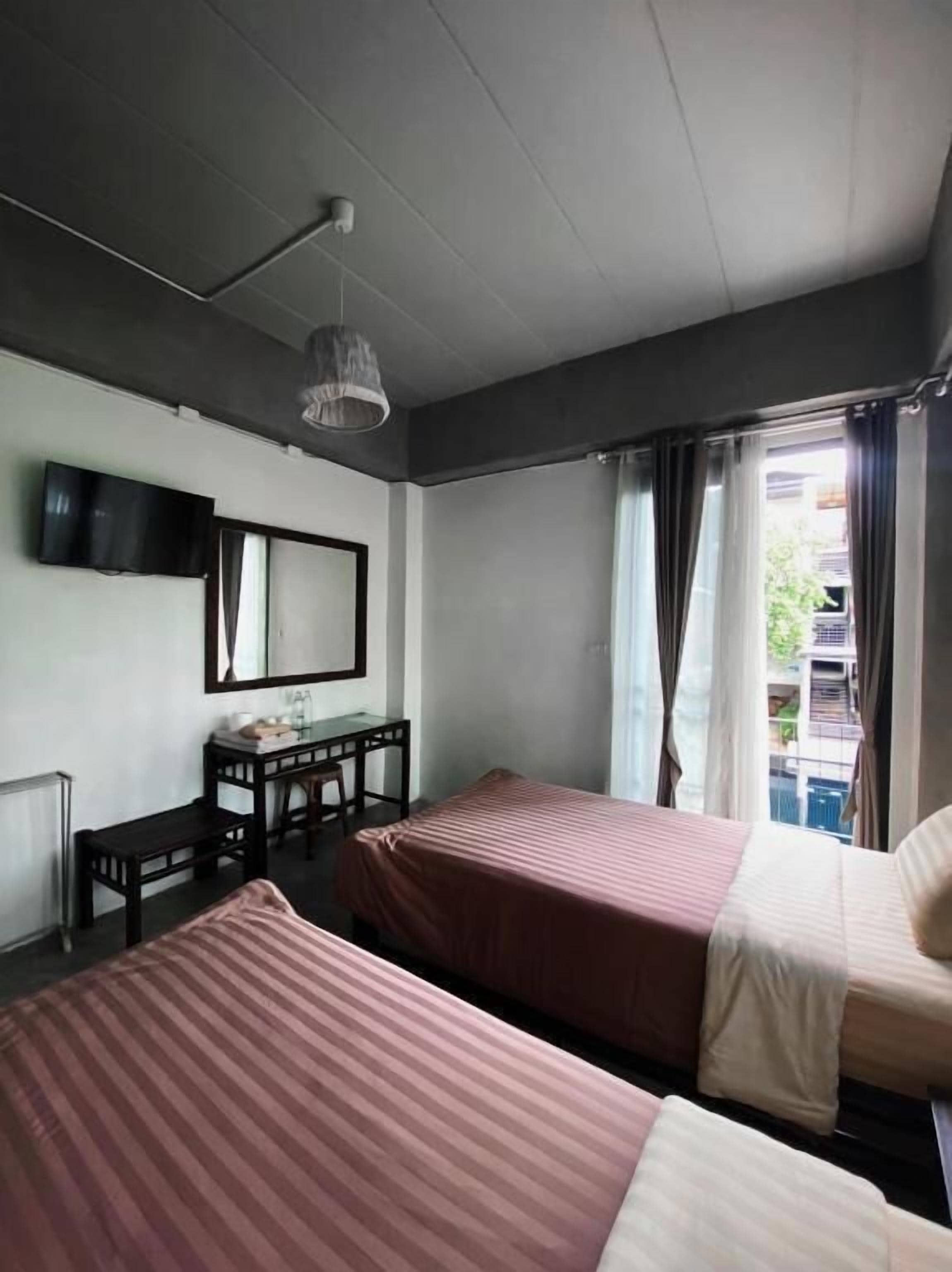 A room with two beds, a desk, a chair, a television, and a window with curtains.