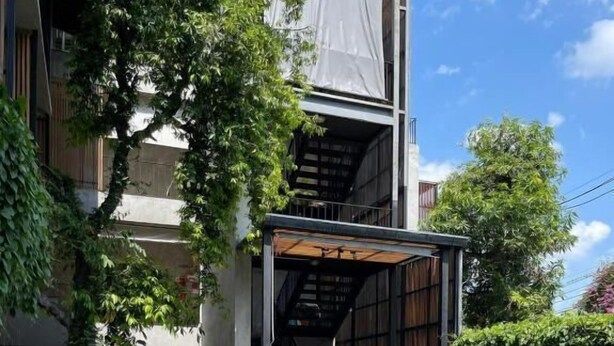 Una mujer sentada junto a una piscina, con un edificio moderno al fondo.