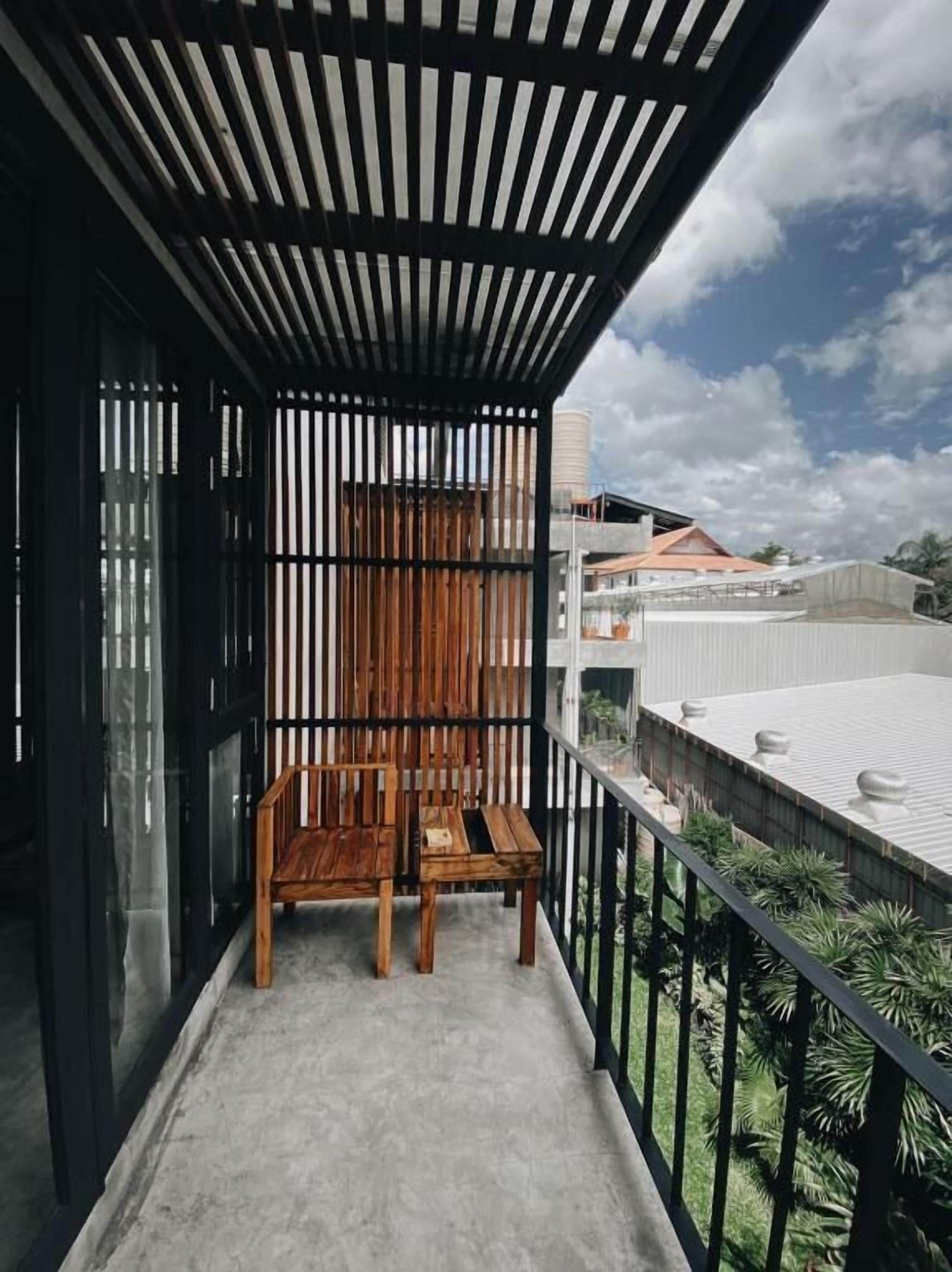 A balcony with a wooden chair and table, a metal railing, and a view of buildings and greenery.