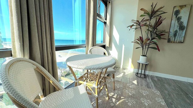 A balcony with wicker chairs, a potted plant, and a view of the ocean. - Tropical Tranquility - Oceanside Retreat w/ Pool (Daytona Beach)