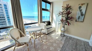 A room with a large window, wicker chairs, a small table, a potted plant, and a beach view. - Tropical Tranquility - Oceanside Retreat w/ Pool (Daytona Beach)