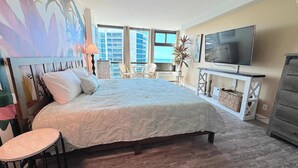 A bedroom with a large bed, a TV, a balcony, and a view of buildings. - Tropical Tranquility - Oceanside Retreat w/ Pool (Daytona Beach)