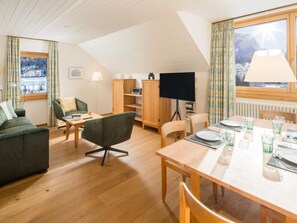 Ein gemütliches Wohnzimmer mit einer Couch, einem Esstisch für zwei Personen und einem Fernseher.