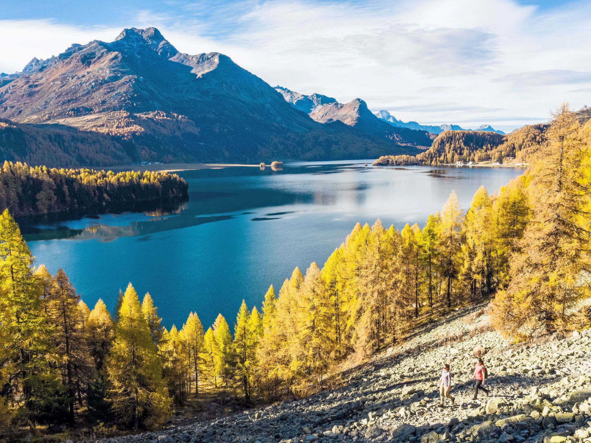 A mountainous landscape with a lake, forested area, and rocky terrain.