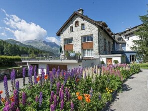 Ein aus Stein gebautes Haus mit einem Balkon, umgeben von bunten Blumen und Bergen im Hintergrund.