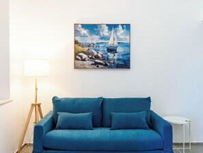 A room with a blue sofa, a painting of sailboats on the wall, a floor lamp, and a small white table. - Apartment Sirena by Interhome (Sanremo)