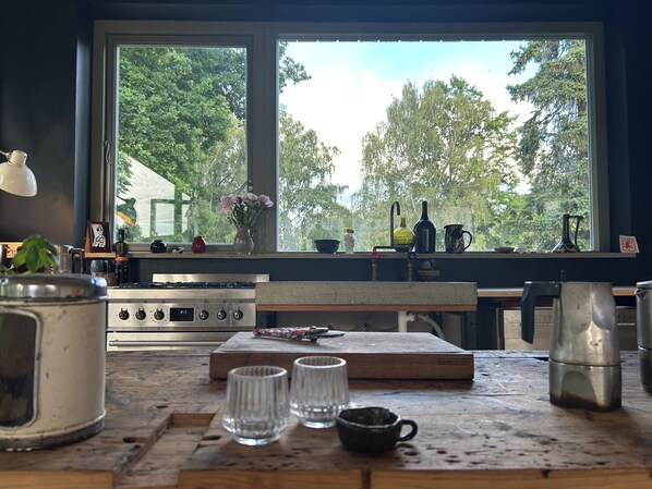 A kitchen with a large window, a stove, a sink, and various kitchen items on the counter.