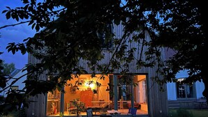 Ett modernt hus med en entré som har en glasdörr, ett matområde med stolar och ett bord samt ett kök som är synligt från resten av huset.