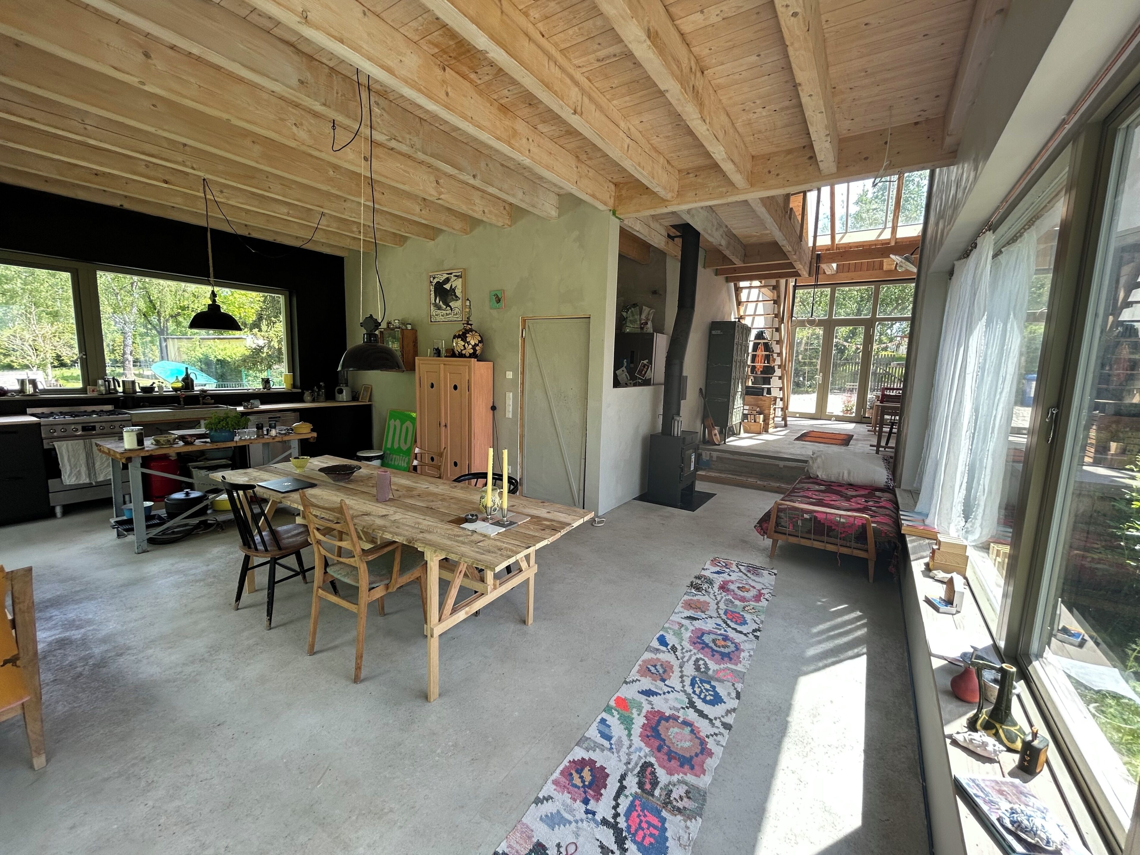 A spacious kitchen with wooden beams, a dining area with a long table, and a large window providing a view of the outdoors.