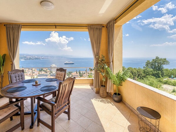 Ein Balkon mit Tisch und Stühlen, einem Blumentopf und Blick auf das Meer und die Stadt.