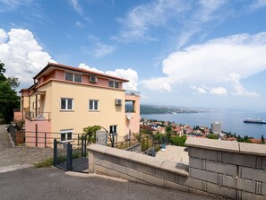 Um edifício de dois andares com varanda, portão e vista para uma cidade costeira e o mar.