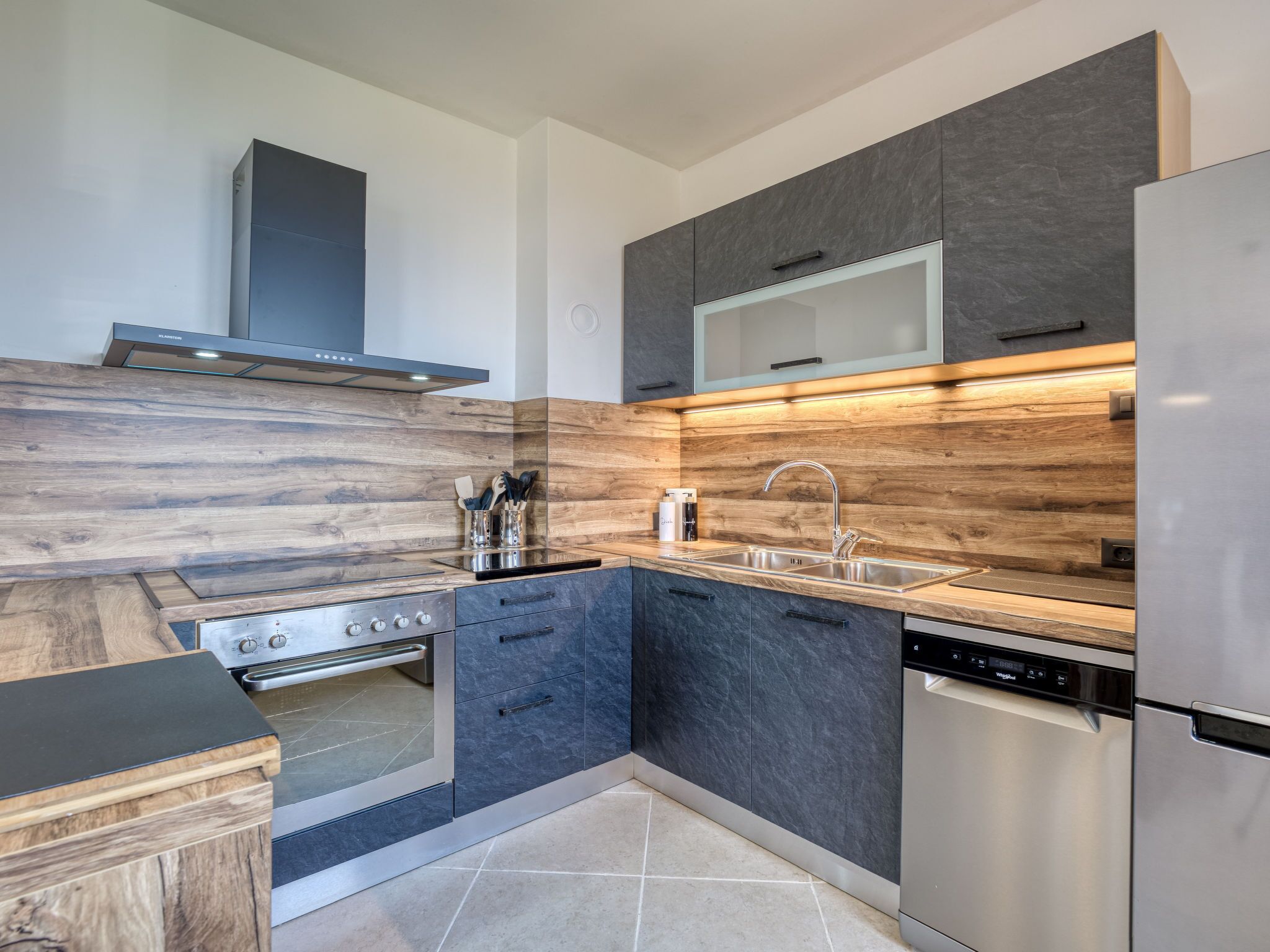 Una cucina moderna con piano cottura, forno e lavastoviglie integrati, caratterizzata da mobili scuri e dettagli in legno.