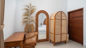 A room with a wooden desk, a wicker chair, a mirror, and a wooden wardrobe. - Casa Vara Uluwatu (Badung)