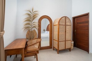 A room with a wooden desk, a wicker chair, a mirror, and a wooden wardrobe. - Casa Vara Uluwatu (Badung)