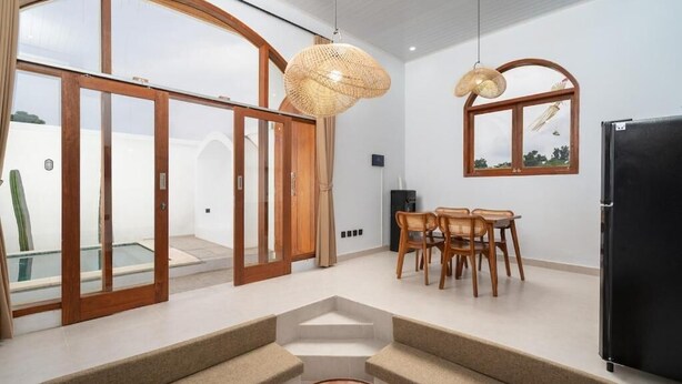 A modern interior with a dining area, sofas, and a large window with a view. - Casa Vara Uluwatu (Badung)
