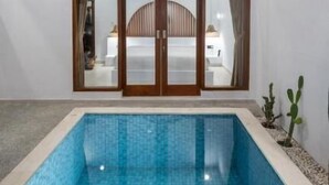 A modern pool area with a glass-enclosed entrance, a clear blue pool, and a wooden ceiling. - Casa Vara Uluwatu (Badung)
