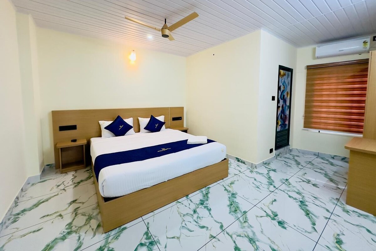A hotel room with a bed, a nightstand, a ceiling fan, an air conditioning unit, and a window with blinds.