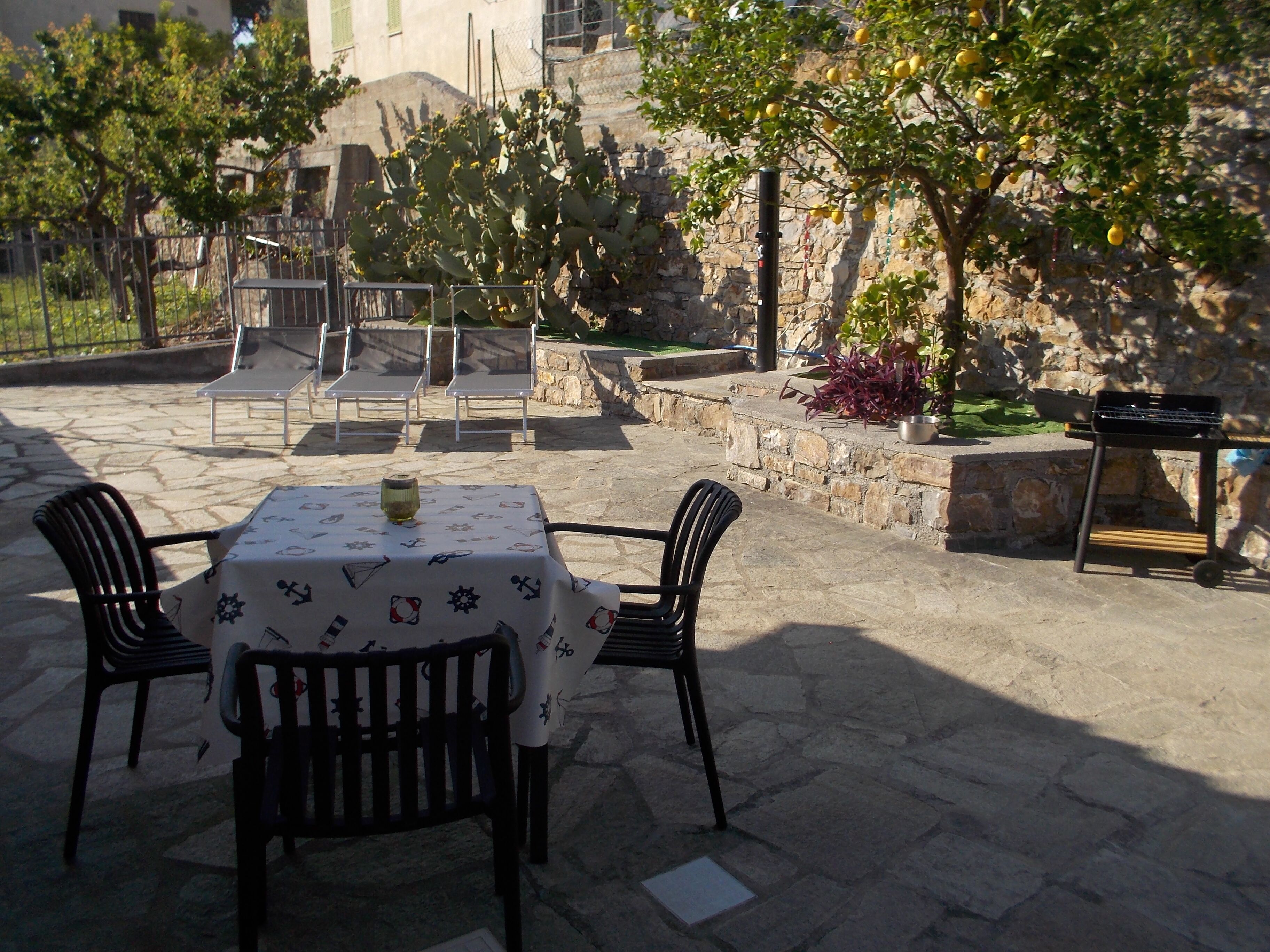 Un patio al aire libre con piso de piedra, una mesa con sillas y una parrilla.