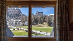 Finestra amb vista a un complexos d'edificis, un prat verd i una muntanya.