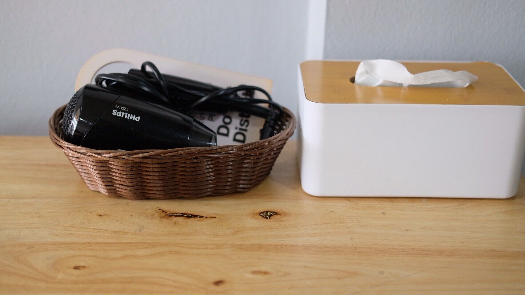 A wicker basket with a black object and a white box with a tissue on a wooden surface.