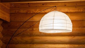 En mysig stuga med träpanel på insidan, en mörkgrå soffa, mönstrade kuddar, en fluffig vit fåtölj och en hängande lampa.