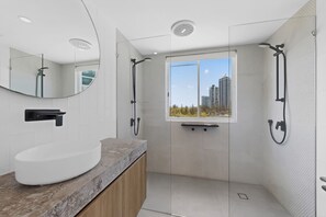 Ein modernes Badezimmer mit einem gebogenen weißen Waschbecken, einem Spiegel und einer Dusche mit Glastür.
