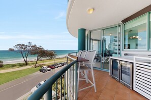 Ein Balkon mit Blick auf den Ozean, eine Essecke mit Stühlen und eine Küchenzeile.
