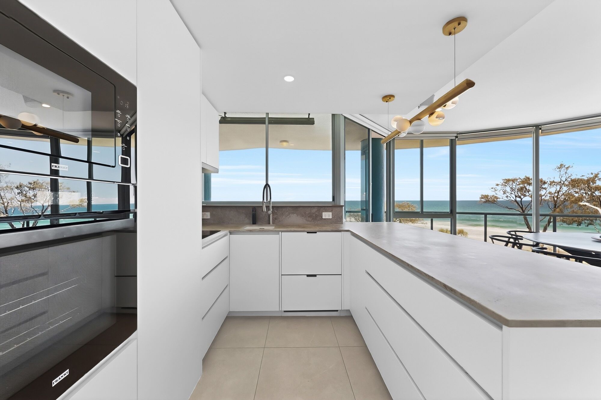 A modern kitchen with a view of the sea, large windows, and a minimalist design.