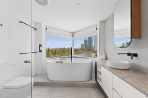 Ein modernes Badezimmer mit freistehender Badewanne, großem Fenster mit Blick auf Stadt und Grünflächen, sowie minimalistischem Design.