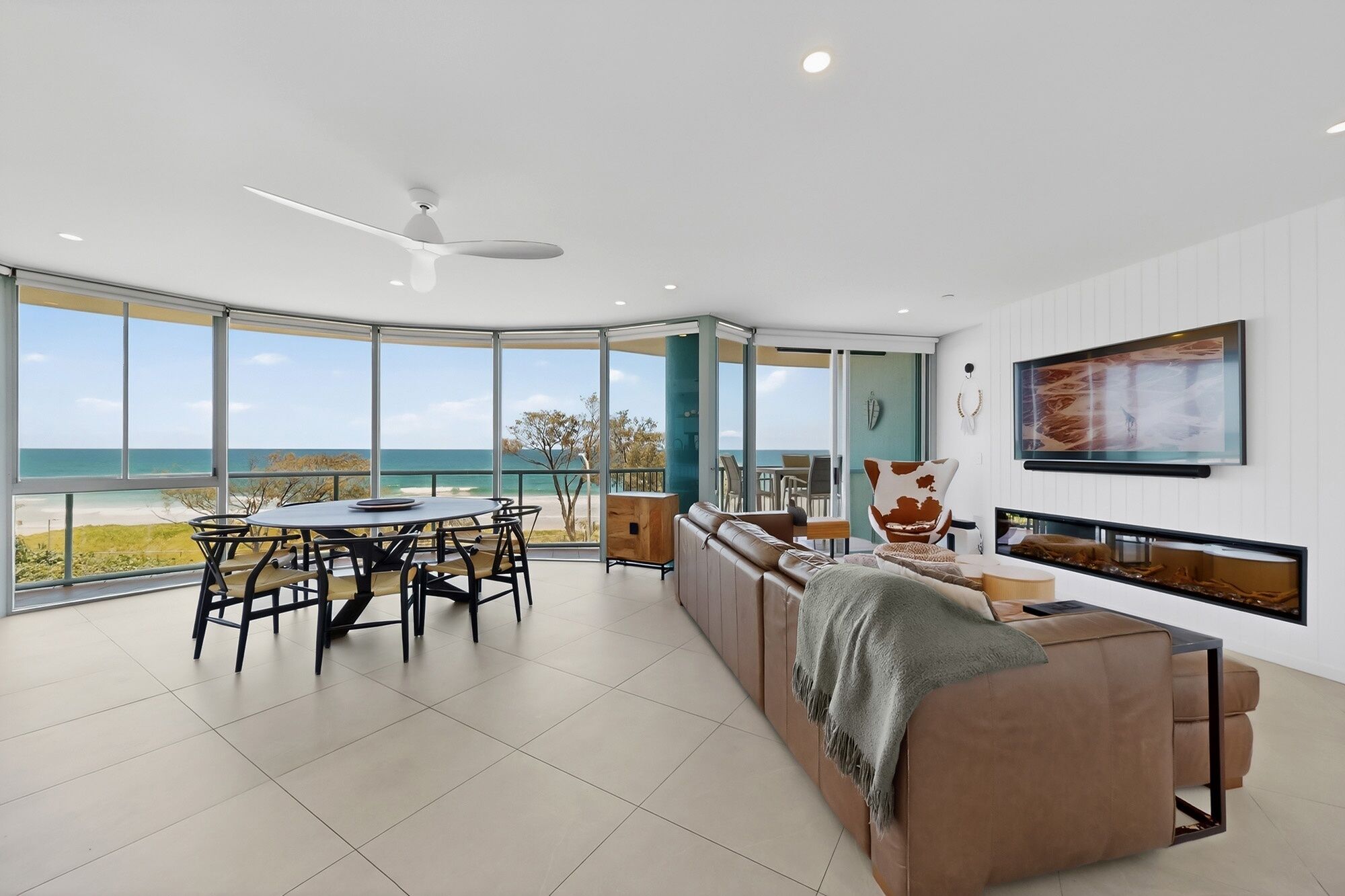 A modern living room with a large panoramic window, a ceiling fan, and a seating area with a sofa and a coffee table.