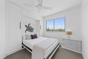 Ein Schlafzimmer mit einem Bett, einem Deckenventilator, einem Fenster mit Blick und einem Nachttisch mit Lampe.