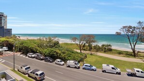 Eine Küstenstraße mit geparkten Fahrzeugen, einem Strand und blauem Himmel.