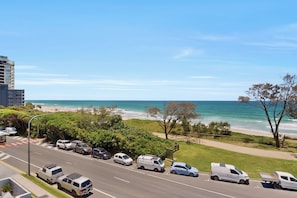 Eine Küstenstraße mit geparkten Fahrzeugen, einem Strand und blauem Himmel.