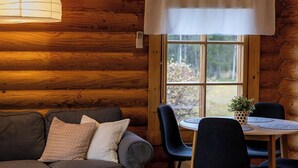 A log cabin interior with a sofa, dining table, chairs, and a window. - Villa Tilhi - Peaceful 2BR Cabin in Ruka (Kuusamo)