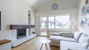 Een moderne woonkamer met een open haard, een bank, een salontafel en een groot raam met uitzicht op gebouwen.