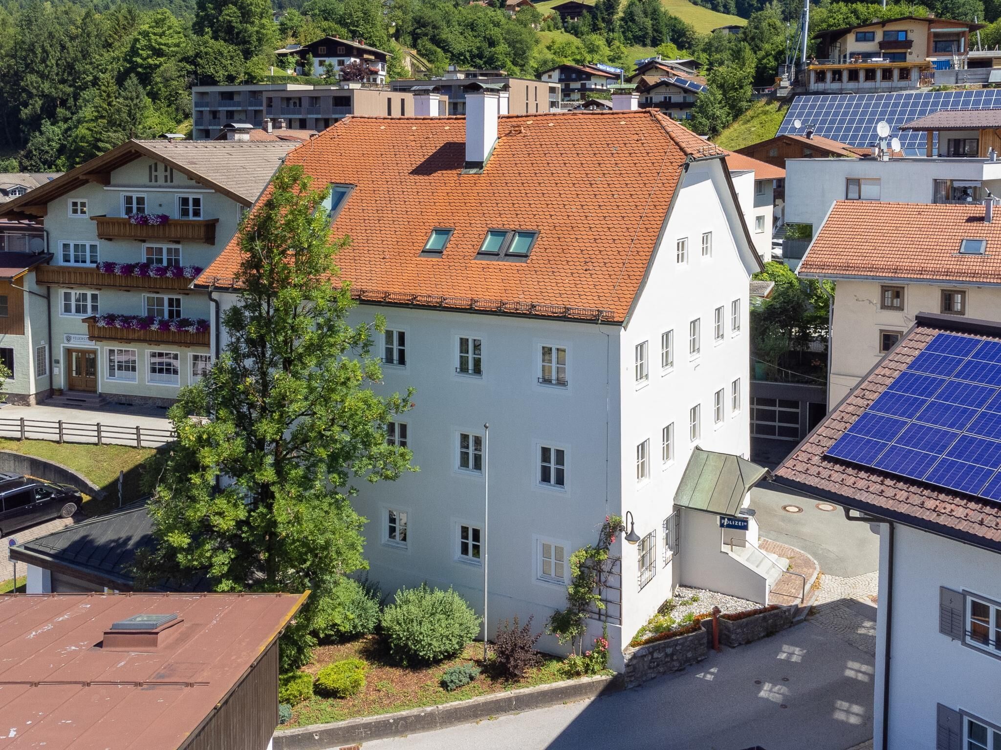 A multi-story building with a red-tiled roof, a balcony with flower boxes, and a solar panel array on the roof.