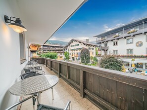 Ein Balkon mit rundem Tisch und Stühlen, Blick auf eine Stadt mit Gebäuden und blauem Himmel.