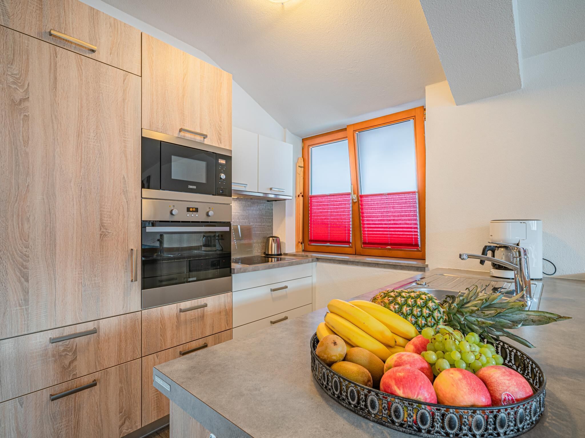 A kitchen with wooden cabinets, a built-in oven, a coffee machine, and a fruit bowl on the counter.