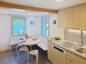 Une cuisine compacte comprenant une table à manger, deux chaises, un évier et une fenêtre donnant sur un espace verdoyant.