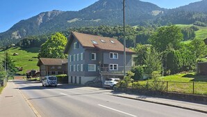 Ein zweigeschossiges Gebäude mit Schrägdach an einer Straßenecke, mit Blick auf eine Bergkulisse.