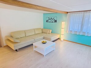 A living room with a beige sofa, a white coffee table with fruit, and a wall with a nature-themed mural. - Ferienwohnung ENZian by Interhome (Lungern)