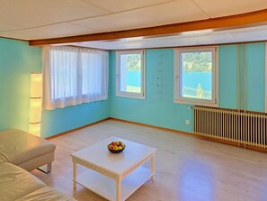 A room with a white table, a sofa, and two windows with curtains.