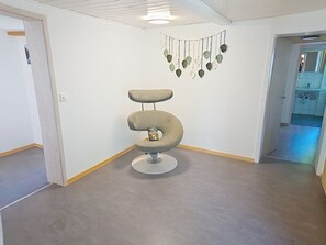 Une pièce avec une seule chaise, un mur blanc, un luminaire au plafond et une porte donnant sur une autre pièce.
