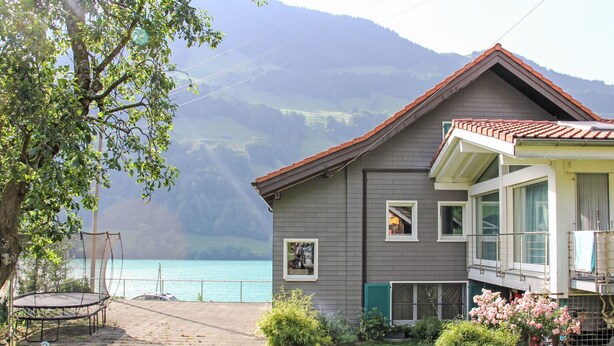 Ein Haus mit Balkon, Blick auf einen See und einem Berg im Hintergrund.