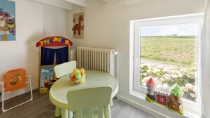 Lasten leikkihuone, jossa on pöytä, tuoleja, patteri, ikkuna, josta on näkymä pellolle, ja leikkimökki, jonka kyltissä lukee ”TEATTERI”.